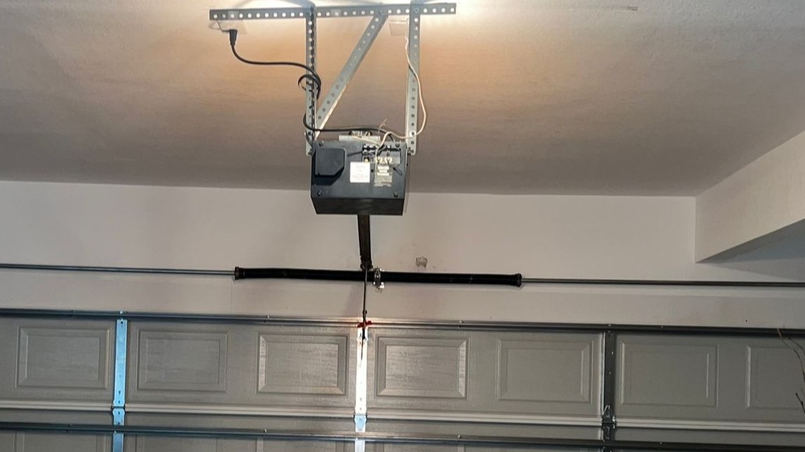 Emergency garage door repair showing an opener and torsion spring system above a residential garage door.