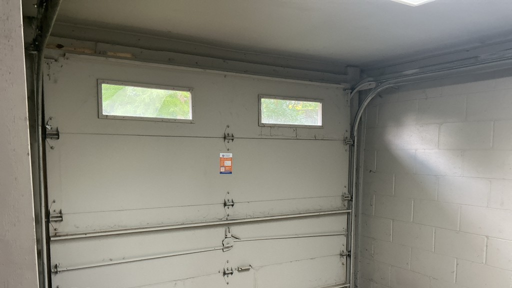 Garage door maintenance in Omaha, NE, showing an older sectional garage door with windows, tracks, hinges, and worn hardware.