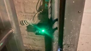 Garage door opener repair in Burbank, CA, showing a safety sensor with a green indicator light near the garage door track.