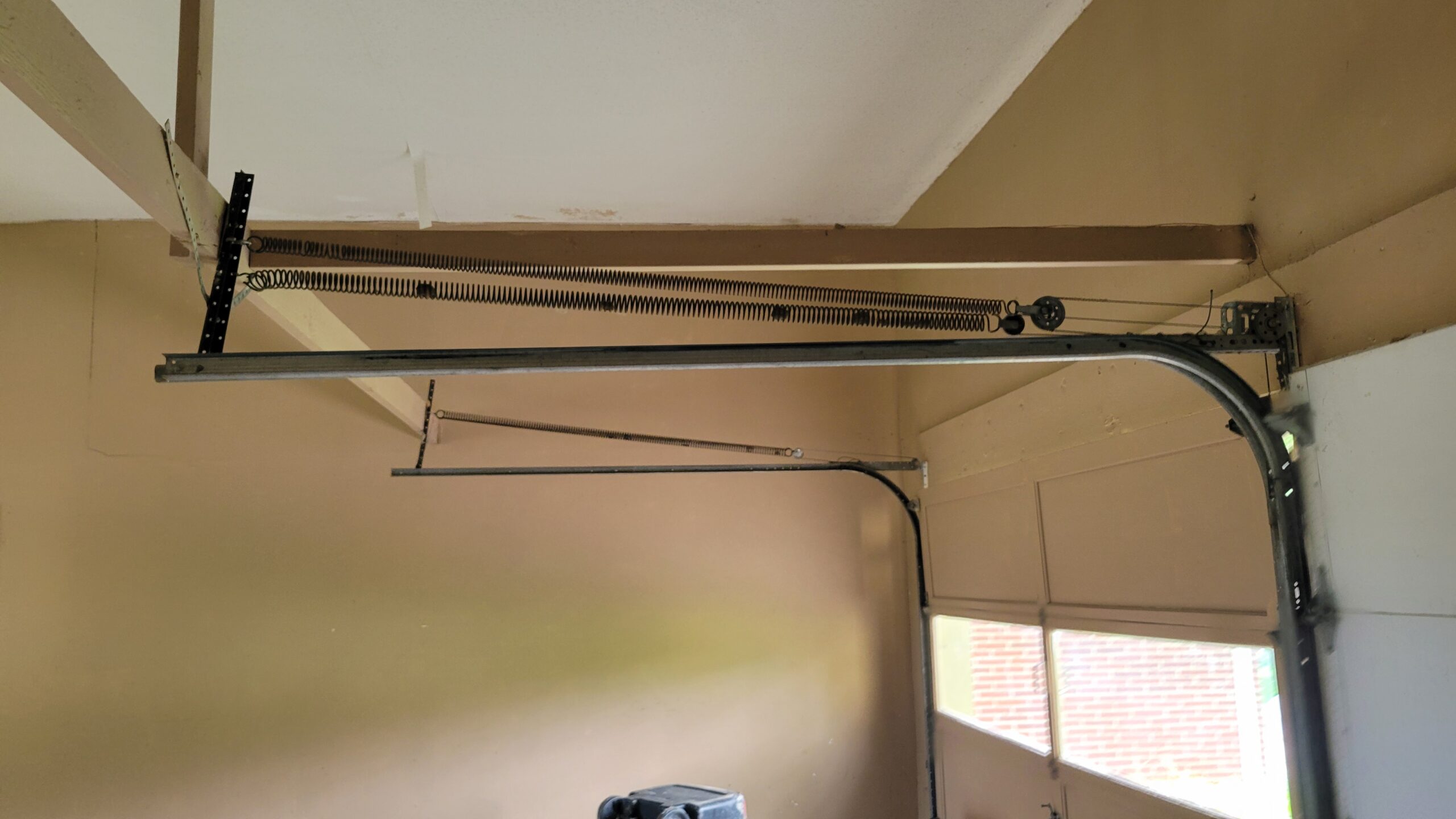 Residential garage door maintenance in Omaha, NE, showing extension springs, pulleys, cables, and overhead track hardware.
