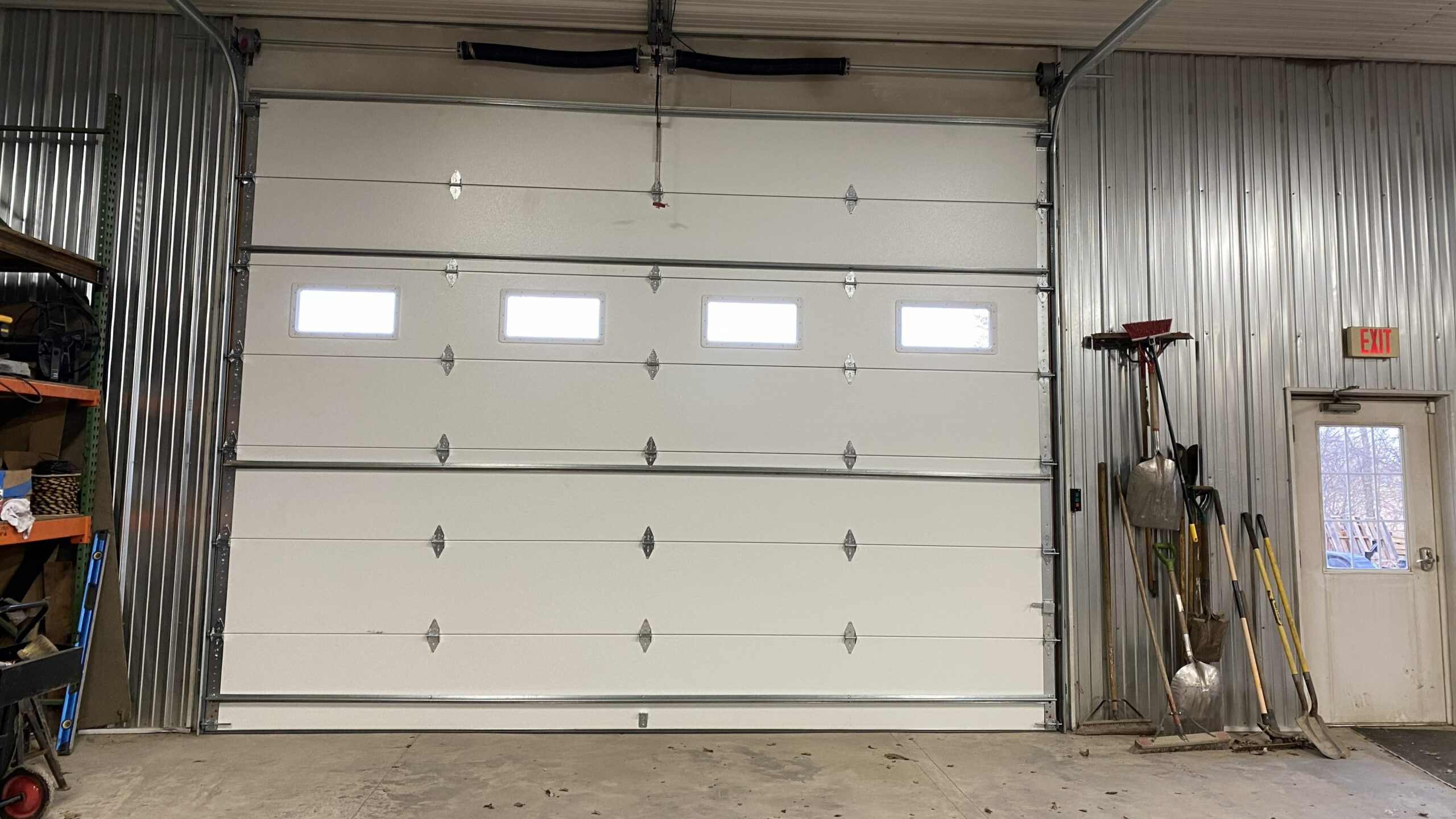 Interior view of a large white sectional garage door with vision windows, torsion spring system, tracks, and commercial-grade hardware after installation in Stoughton, WI.
